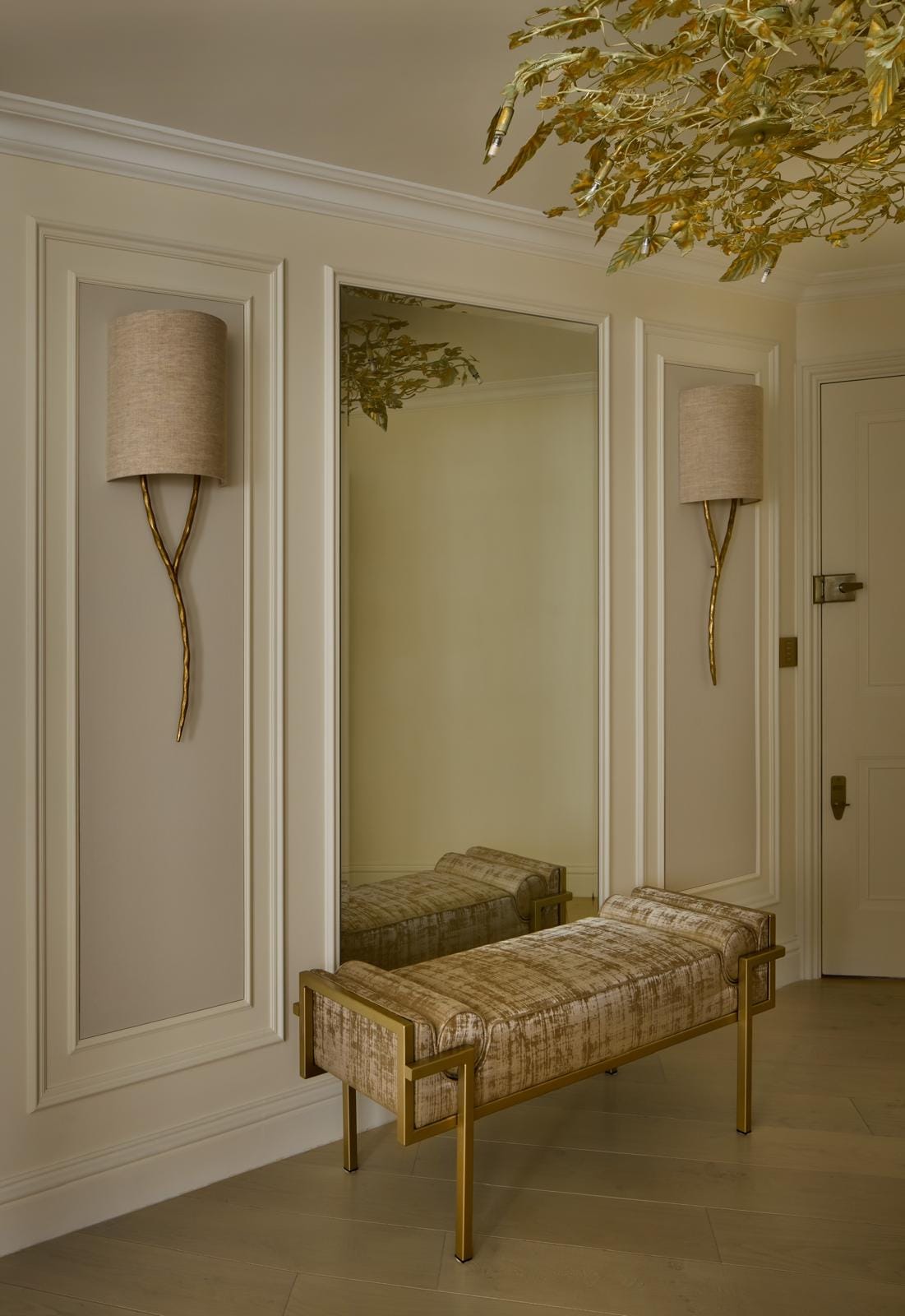 Entrance hall with paired wall sconces, an upholstered bench and a full-height mirror.