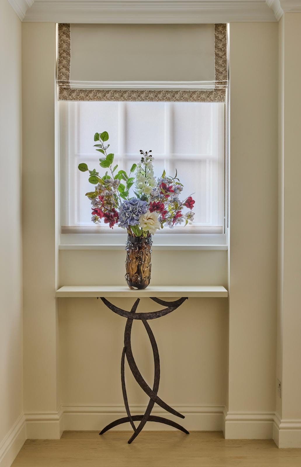 A window nook with seasonal flowers arranged on a sculptural wrought-iron console.