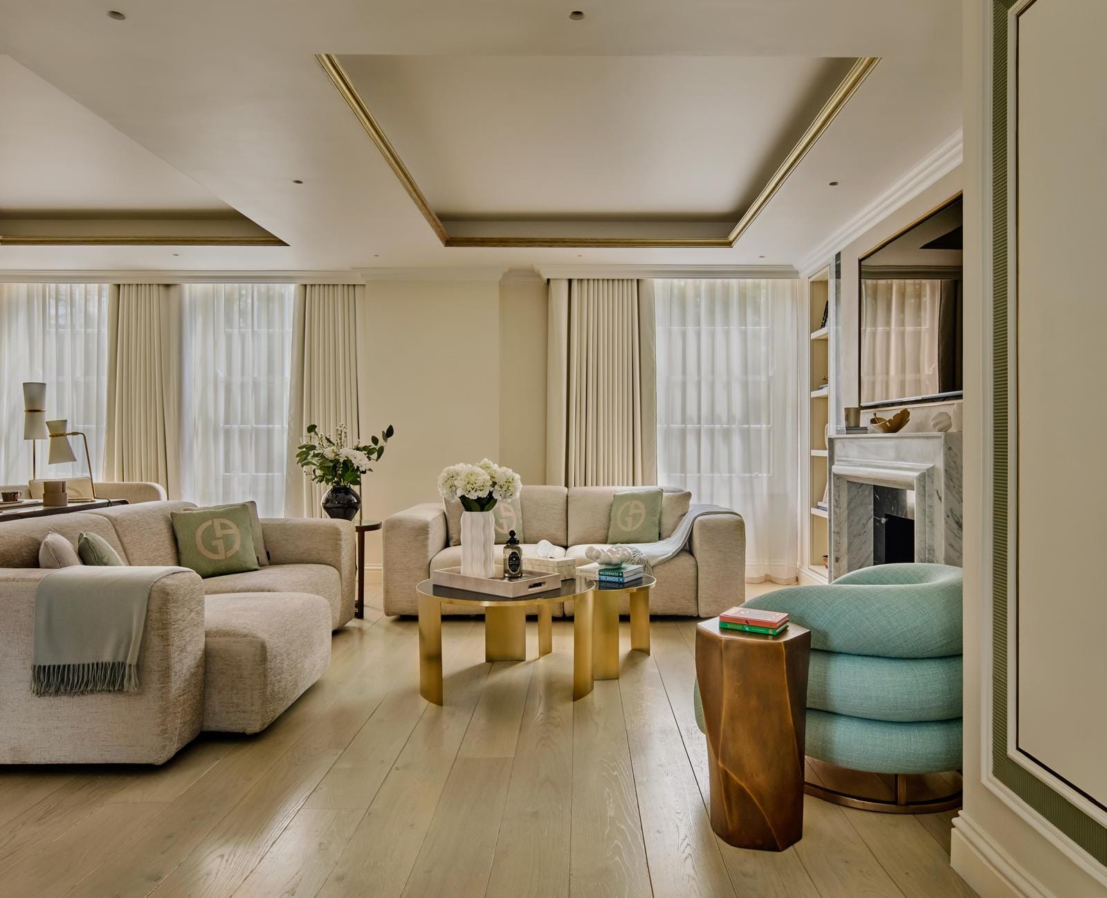 Reception room with bespoke sofas, brass tables and an aqua accent chair beside tall windows.