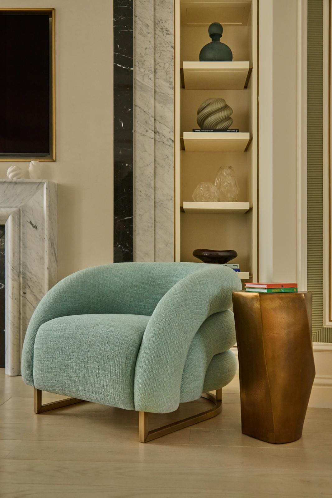 A sitting-room corner with a curved aqua armchair beside a faceted bronze side table.