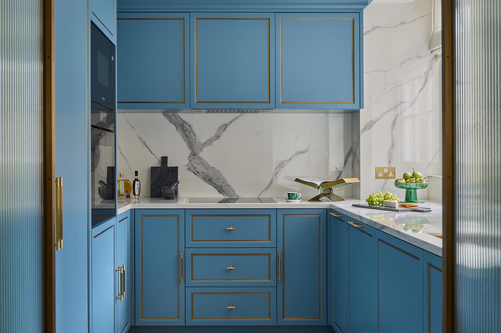 Kitchen in soft blue cabinetry with a book-matched marble backsplash and brass detailing.