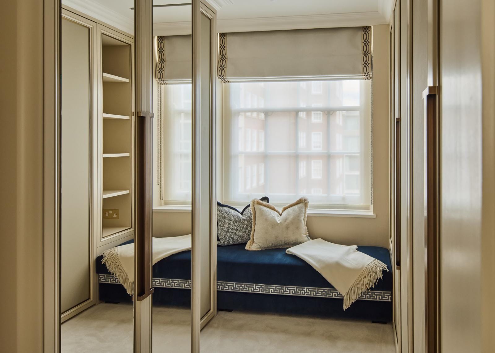 Dressing area with mirrored wardrobes and a deep-blue upholstered window daybed.