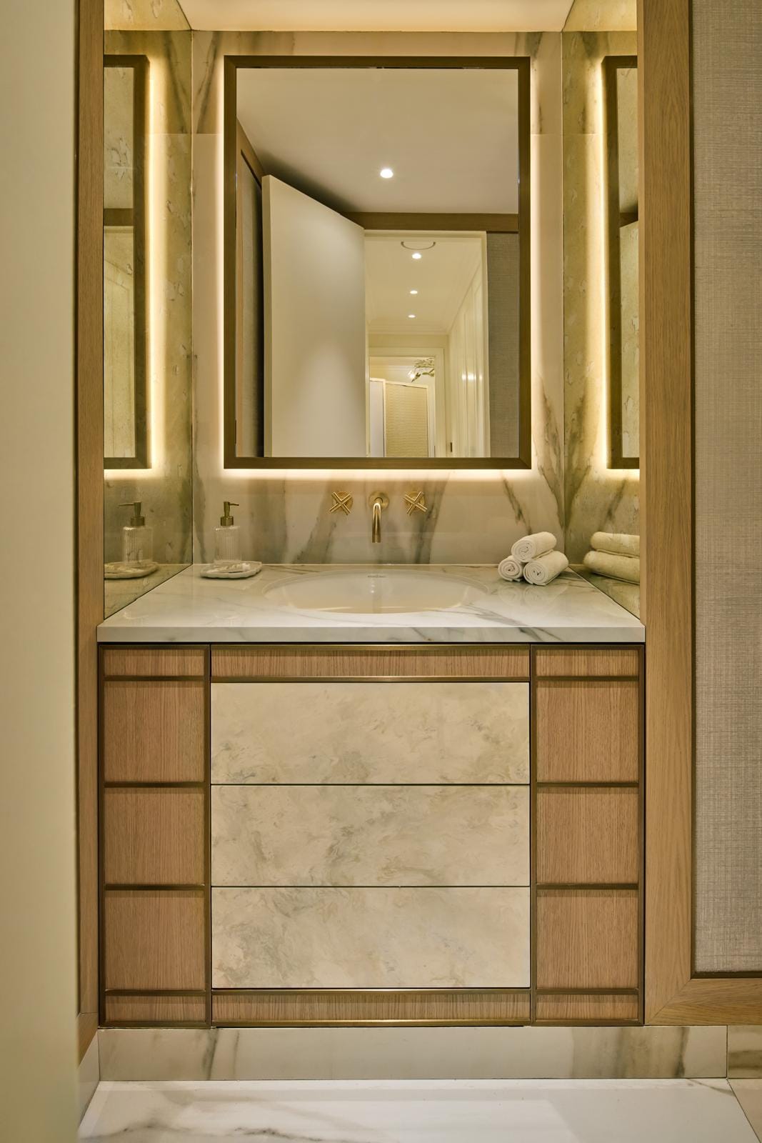 Principal bathroom vanity in marble and oak beneath a softly backlit mirror.