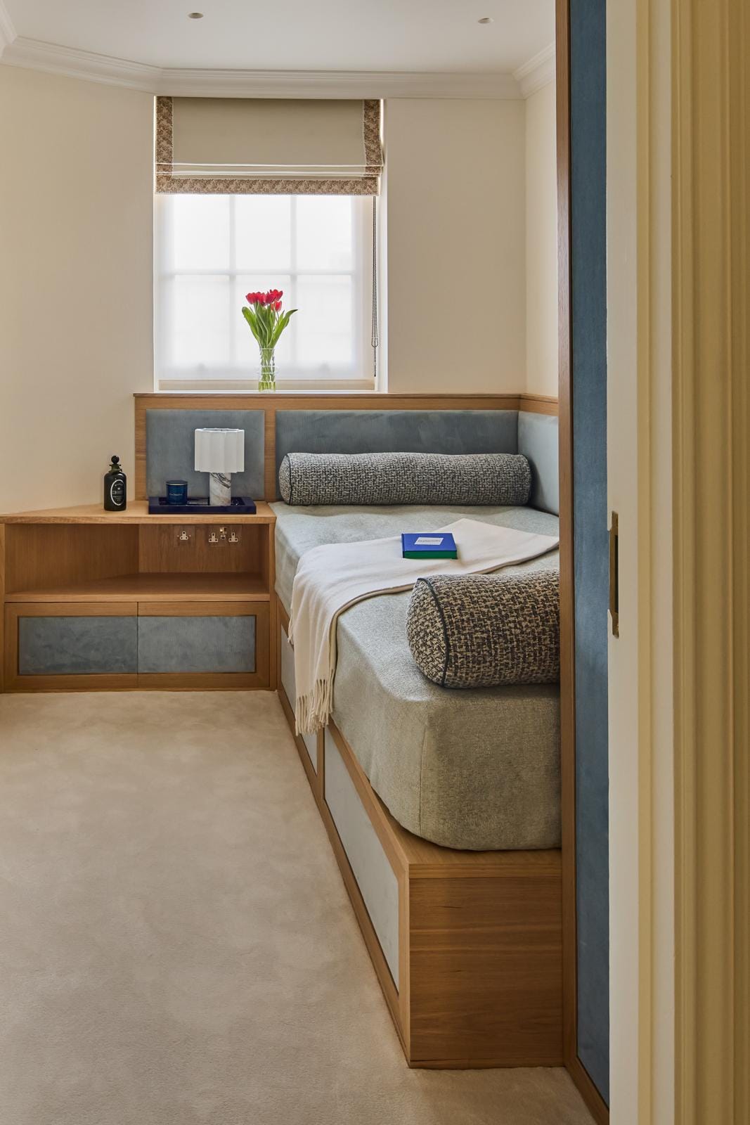 A bedroom with bespoke oak joinery, soft grey upholstery and a built-in headboard.