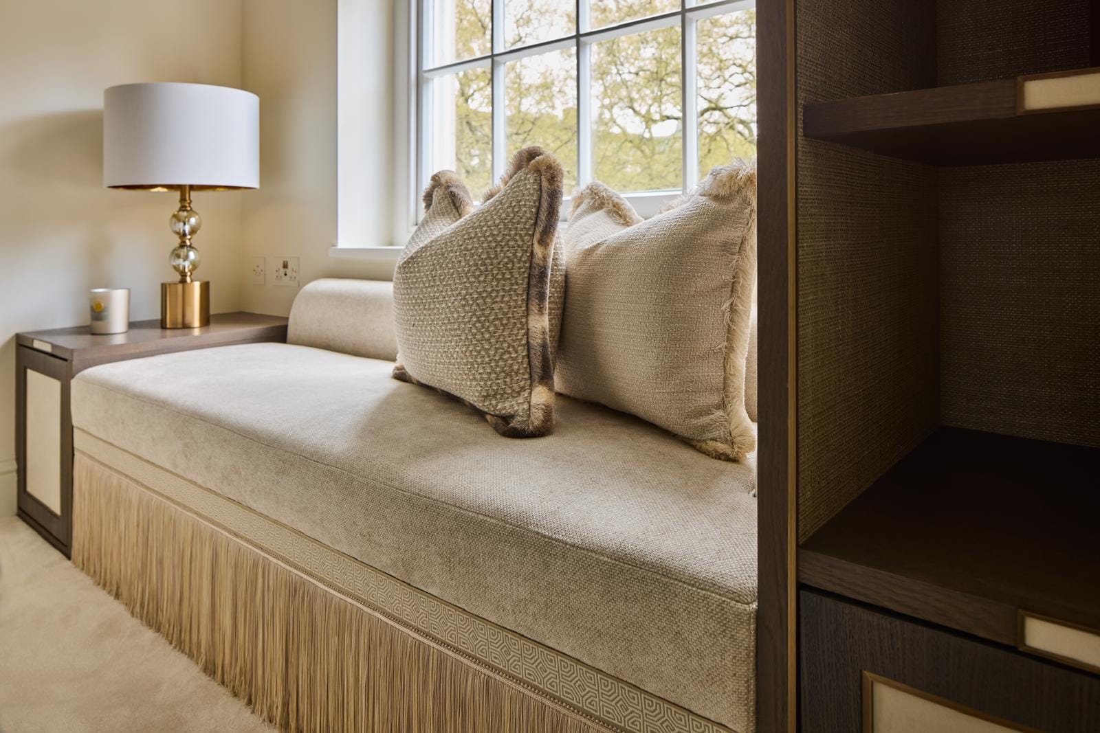 A window seat dressed with fringed cushions in the soft afternoon light.